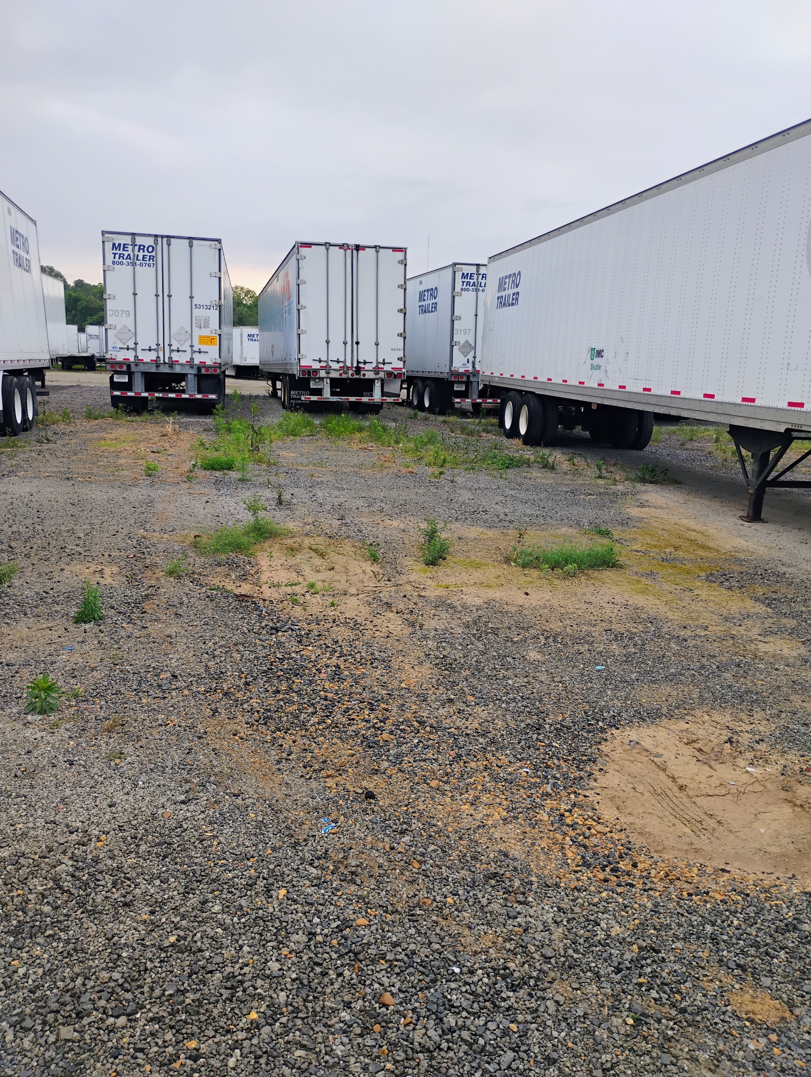 Several white Metro Trailer semi-trailers parked in a gravel lot under an overcast sky.