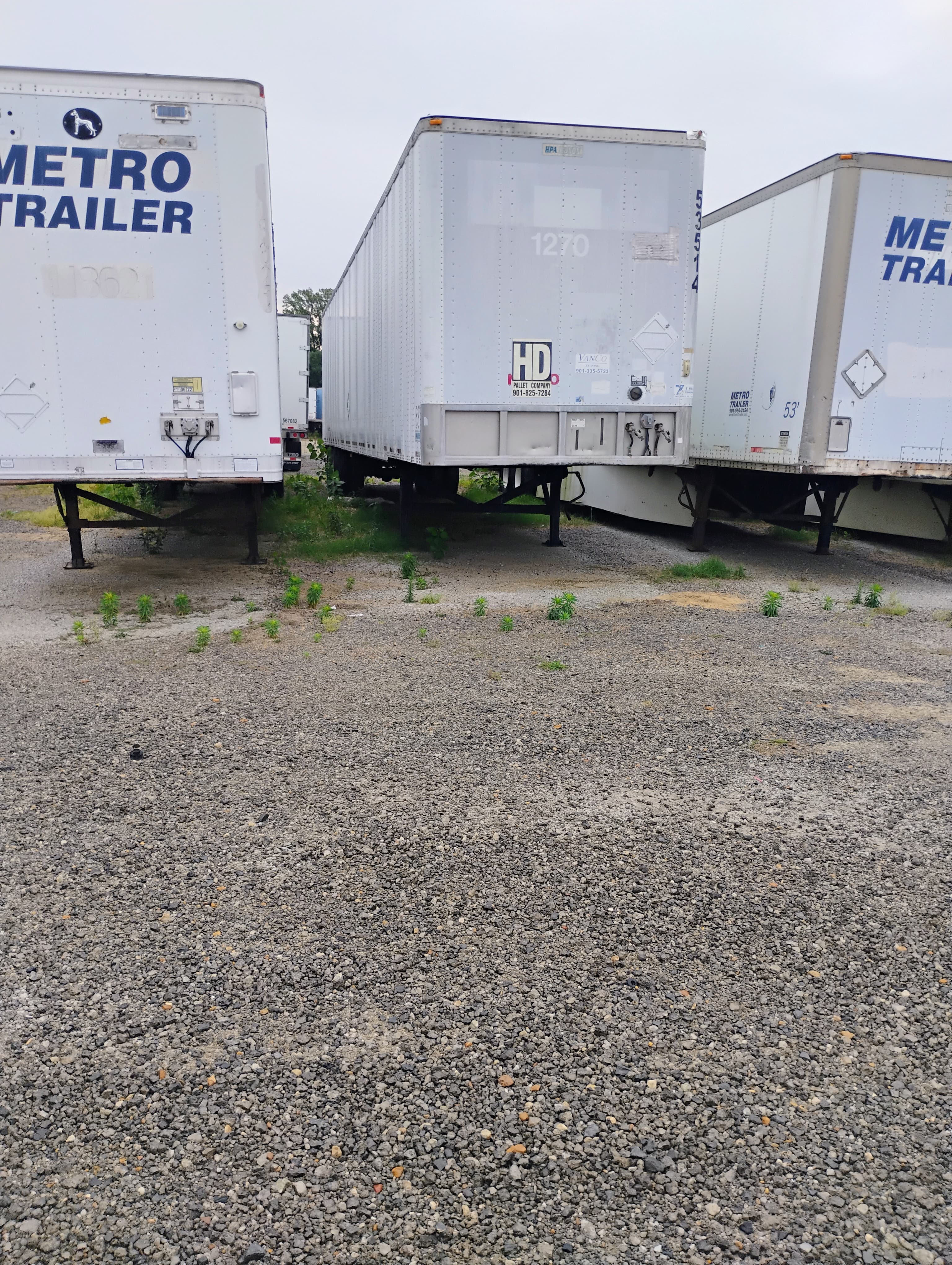 Three white semi-trailers from Metro Trailer and HD Pallet Company parked on a gravel lot.